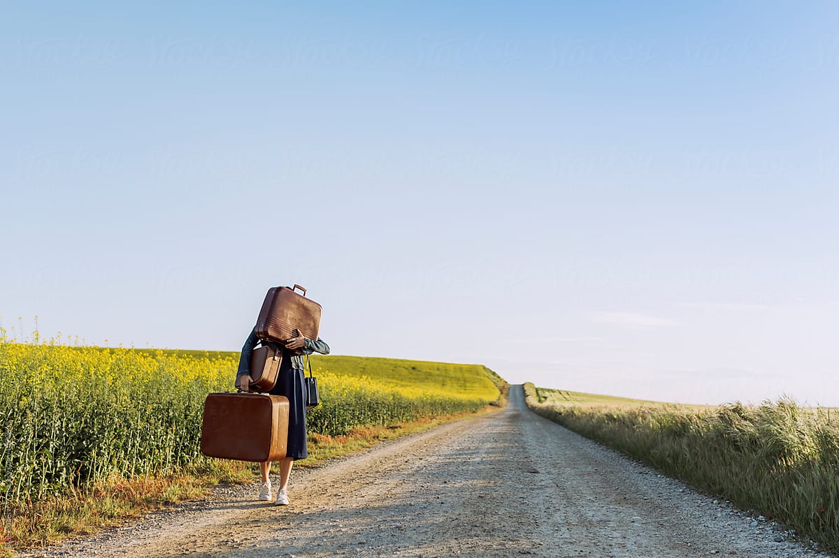 Young Woman carrying many vintage suitcases on a road at springtime