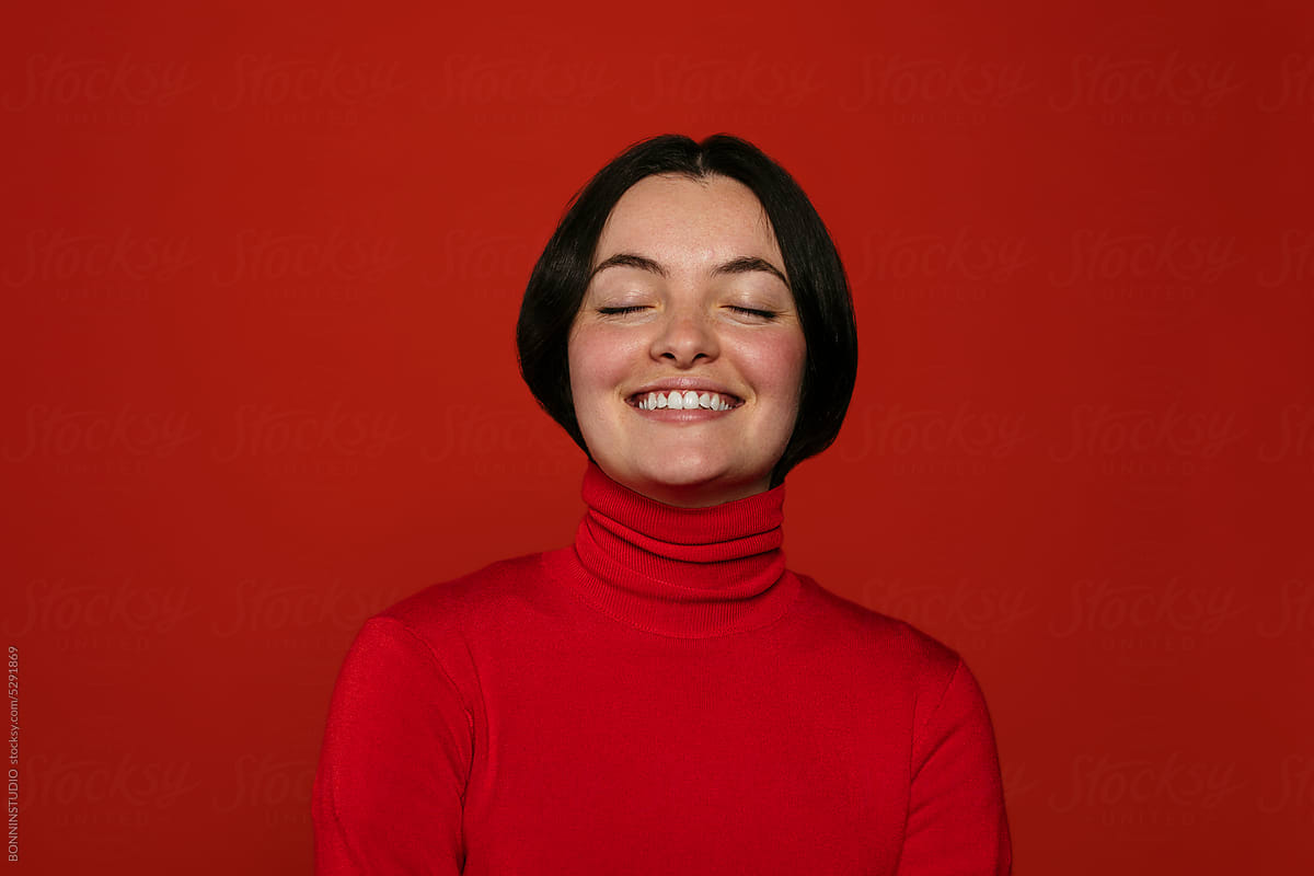 Smiling woman with eyes closed on red background
