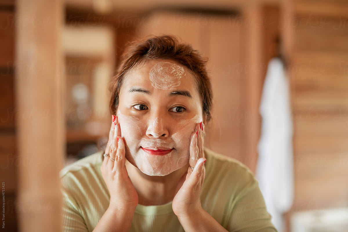 Woman applying foam cream to face reflect with bathroom mirror.