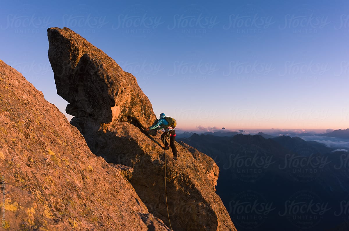Rock climber reaching for the summit of Piz Badile in The Swiss Alps