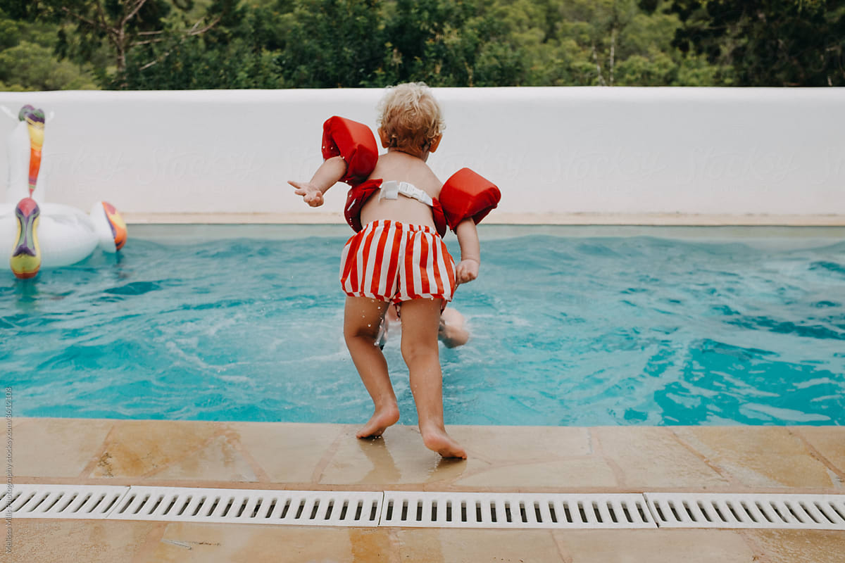 a little boy standing in front of a pool, ready to jump and learn how to swim