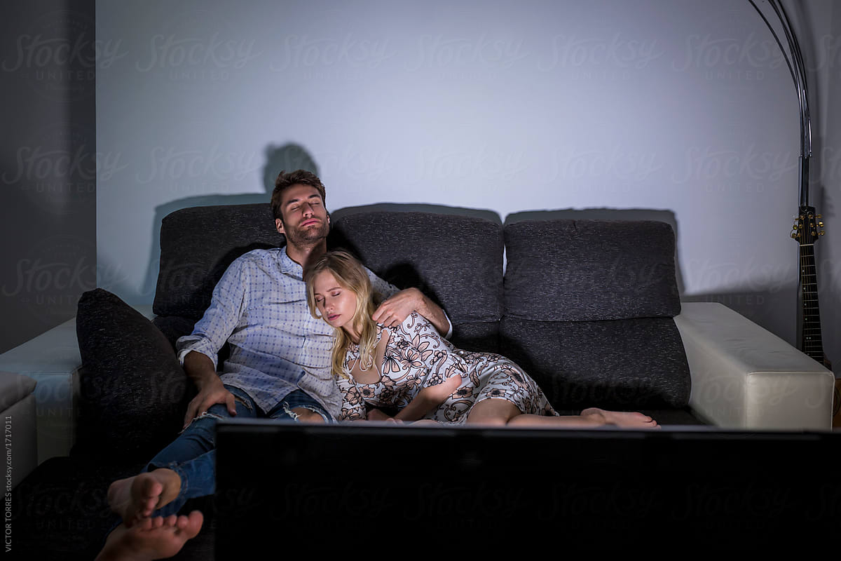 Young couple sleeping on the couch while watching TV at home