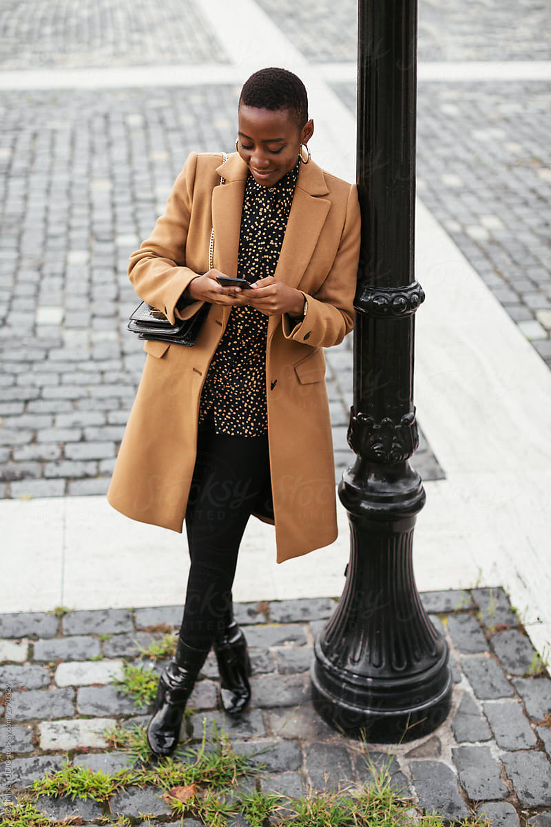 Stylish ethnic woman texting on smartphone on urban street