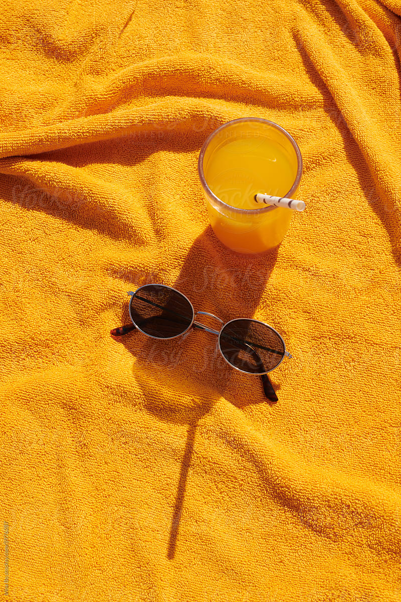 sunglasses and orange juice in a glass stands on an orange towel
