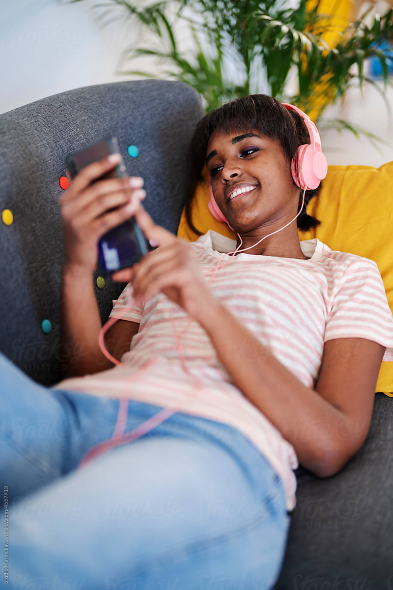 Cheerful black woman listening to music on couch