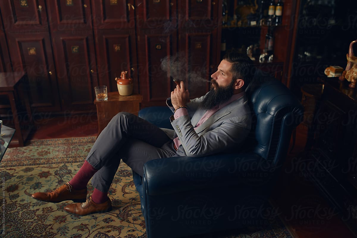 Handsome Man with beard sitting in chair and smoking cuban cigar.