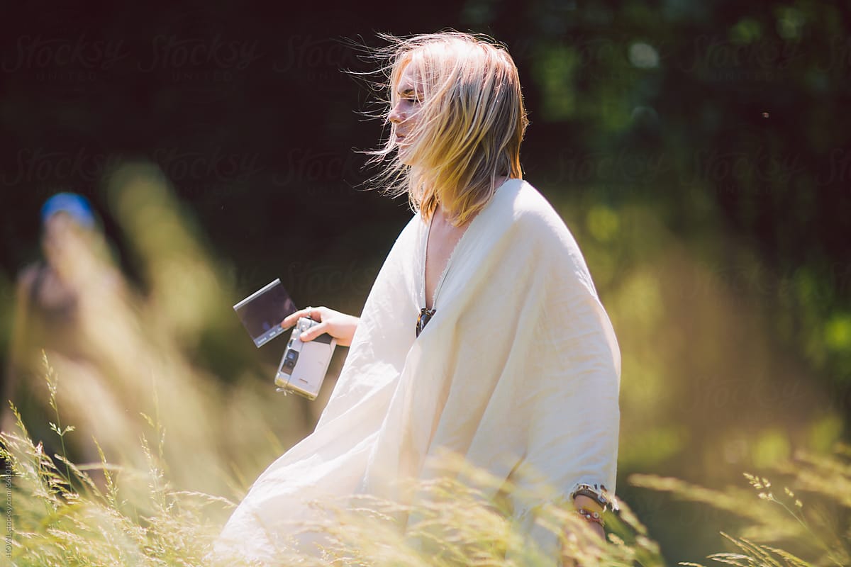 A young female photographer strolls through a sunlit meadow with her camera