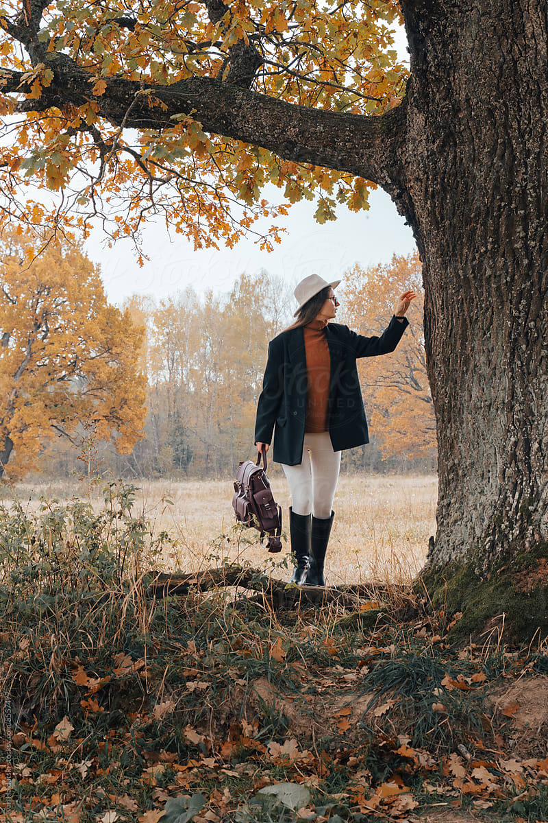 Young thoughtful woman in fall attire hikes touch oak tree