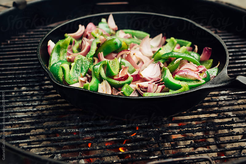 Peppers and onion roasting in a skillet over a grill