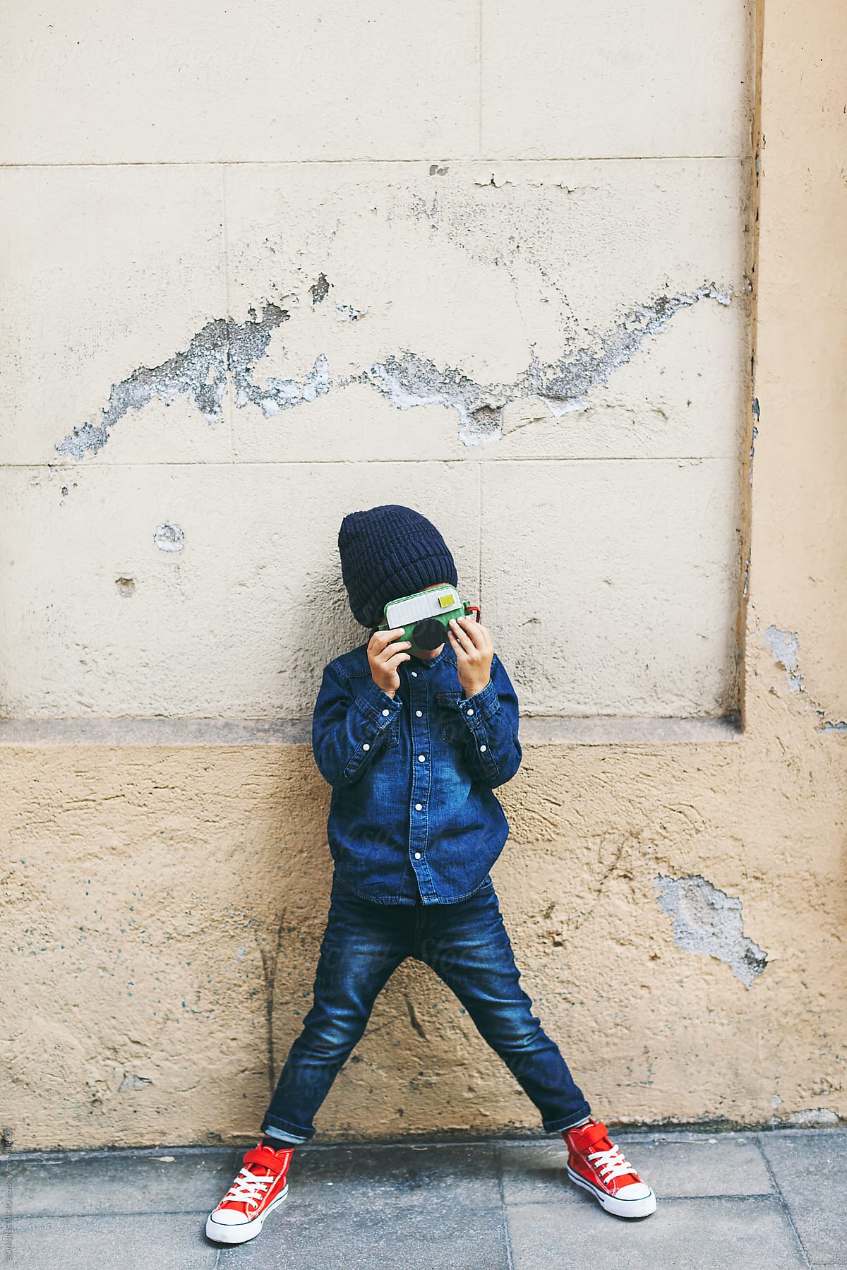 Little boy wearing denim clothes with diy camera. Child standing in front a wall on street.