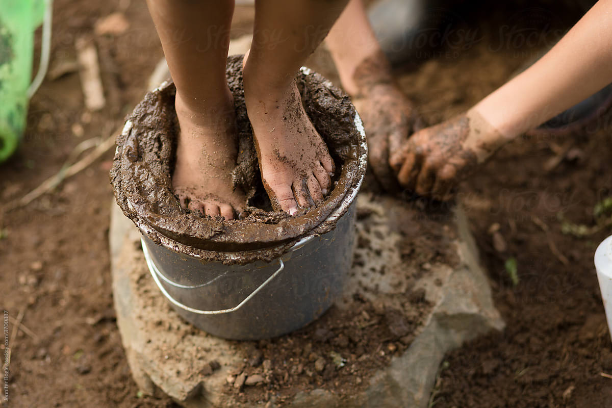 Child stands in bucket of mud