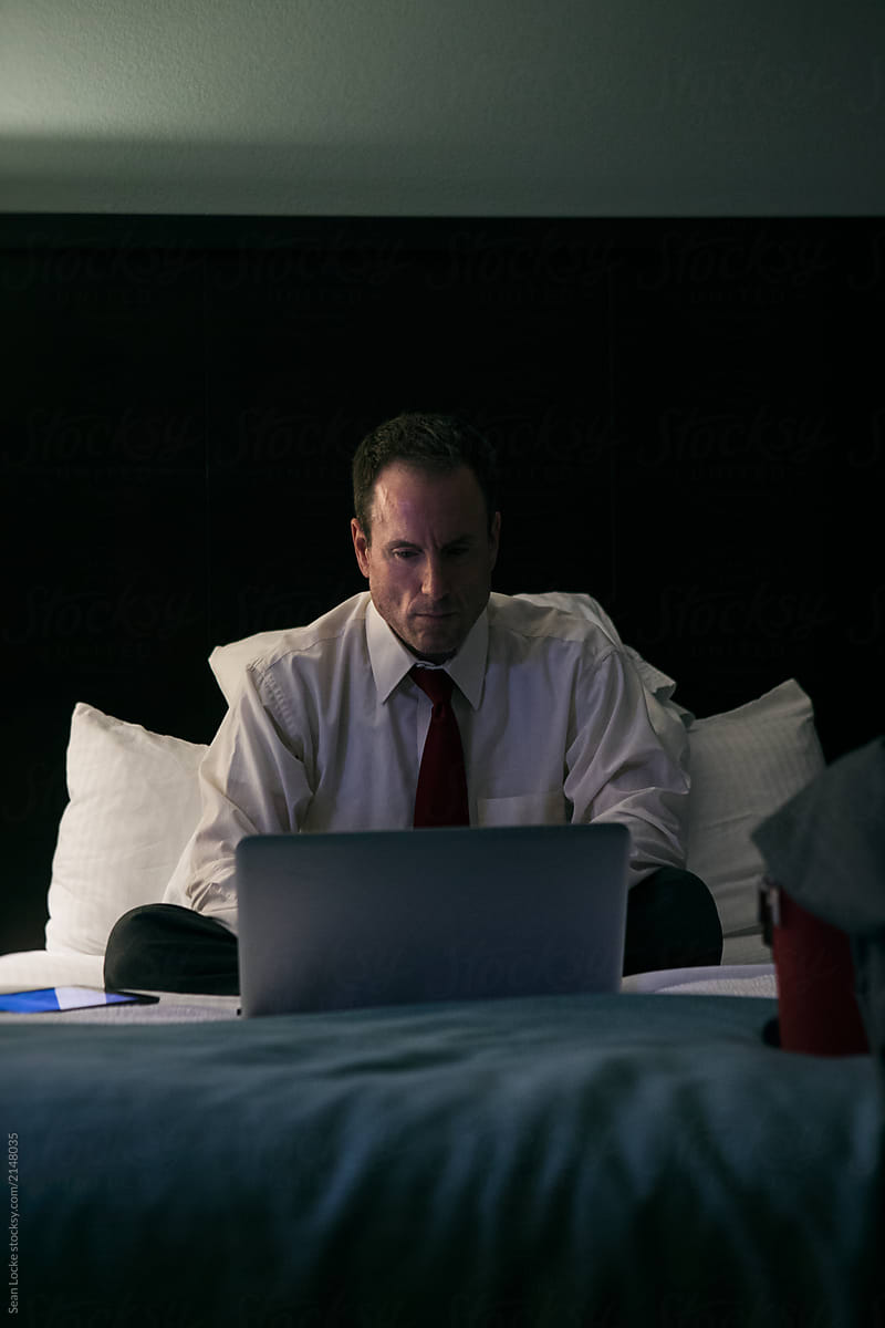 Business: Man Works On Laptop In Bed After Traveling