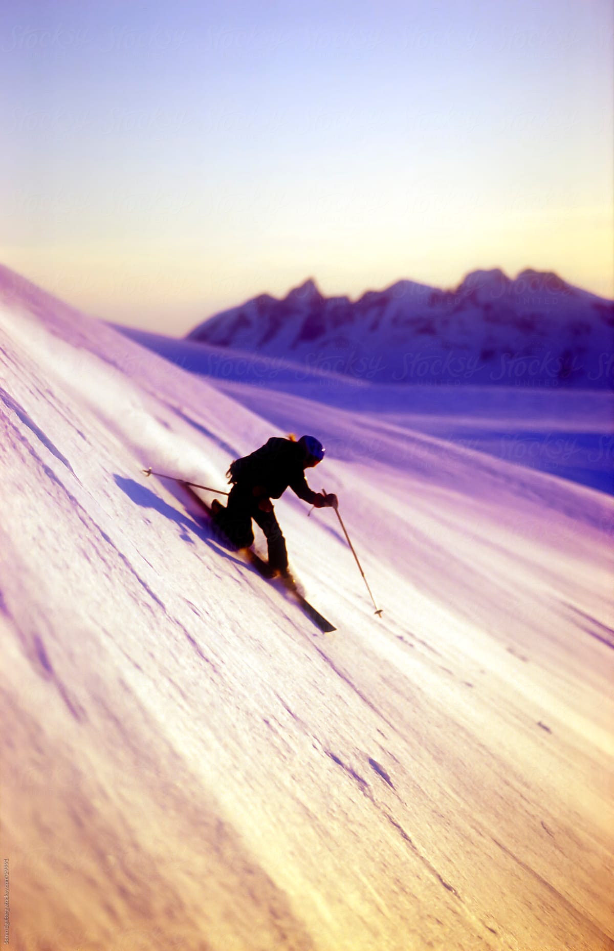Young adult female skier skiing a steep snow slope at sunset