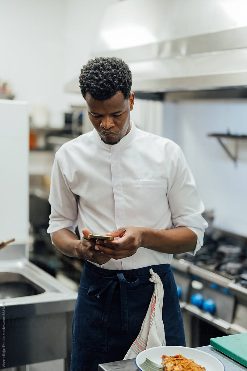 Black chef using smartphone in kitchen in restaurant