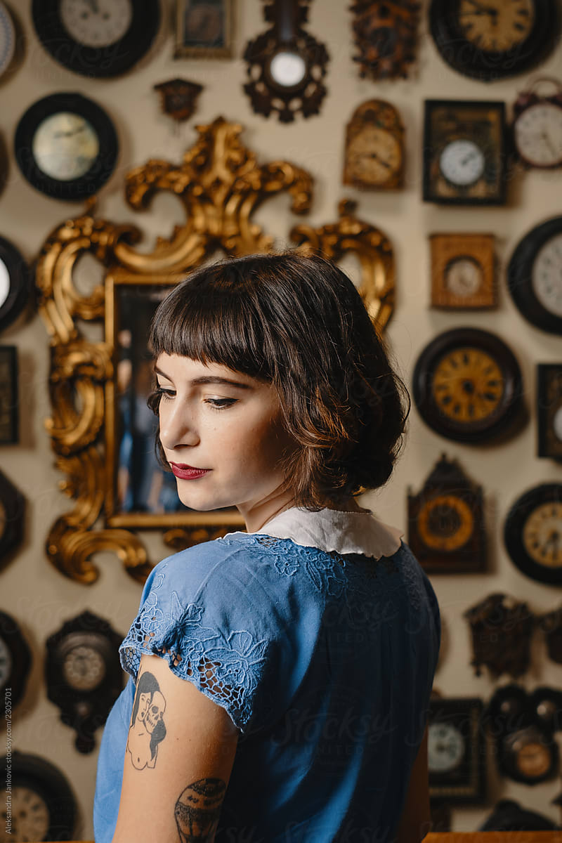 Portrait Of Stylish Tattooed Woman In Front Of The Wall With Clocks