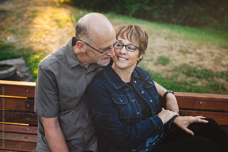 Middle Aged Retired Couple Kissing And Cuddling Outside Sitting On A Bench By Rob And Julia