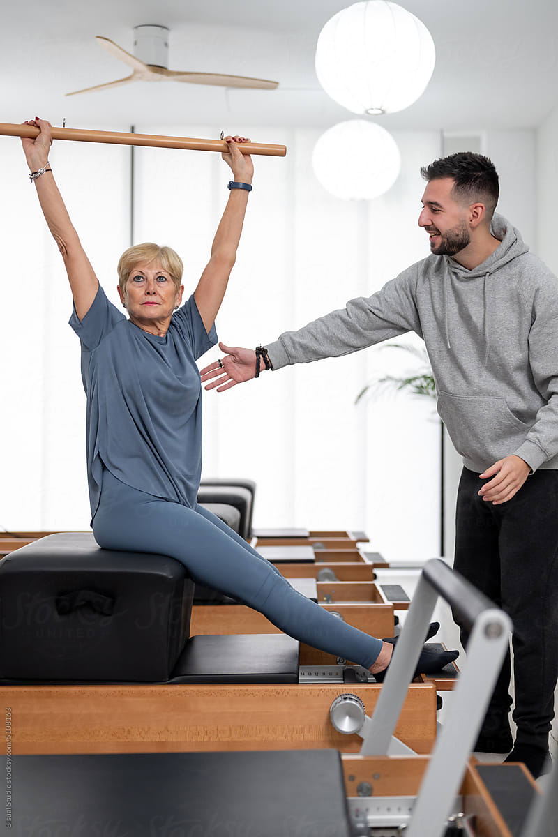 Mature female exercising with Pilates stick with coach