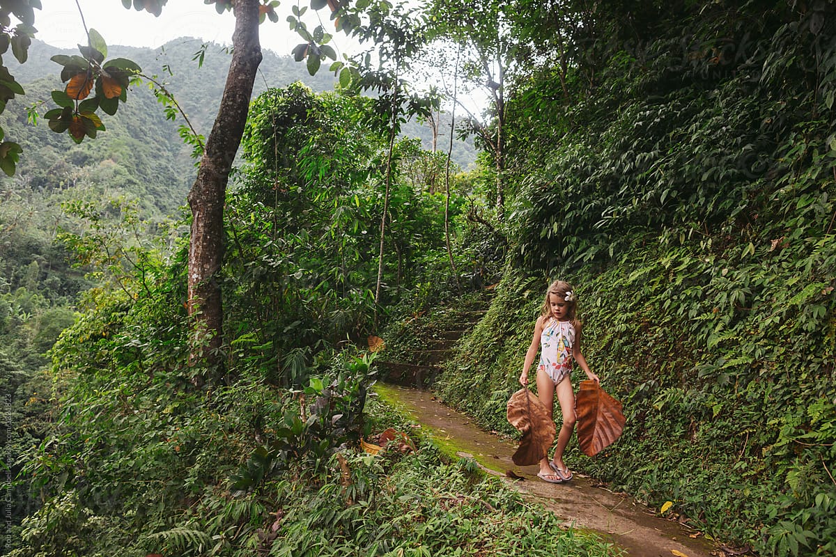 Little girl walking on lush trail holding big tropical leaves