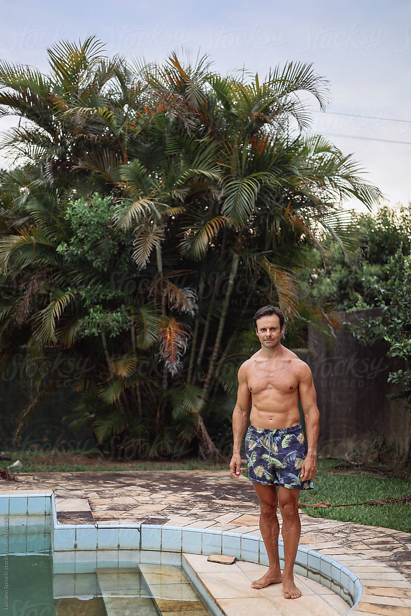 Man standing next to the swimming pool and the palm trees