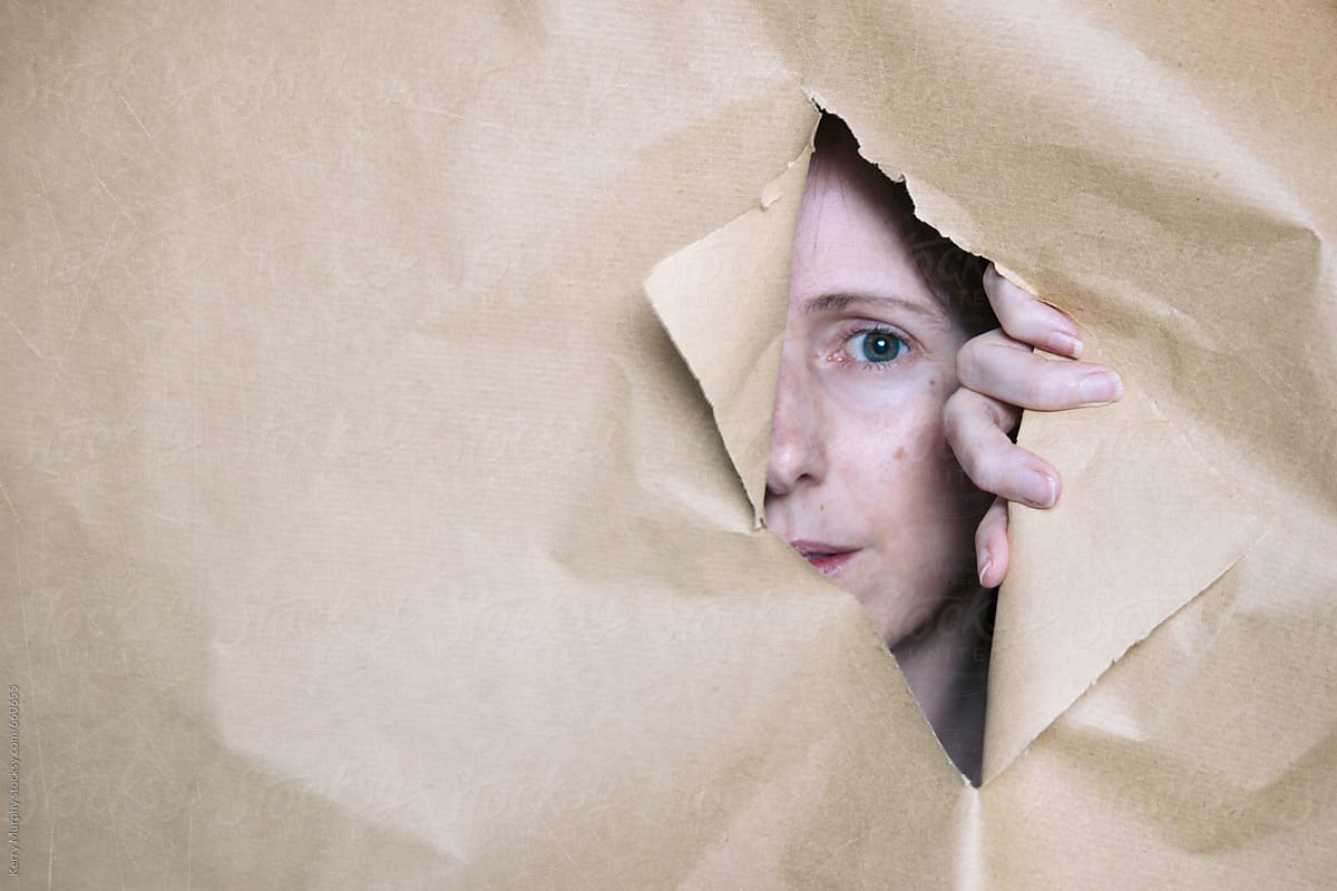 Partial woman\'s face looking through hole in torn paper
