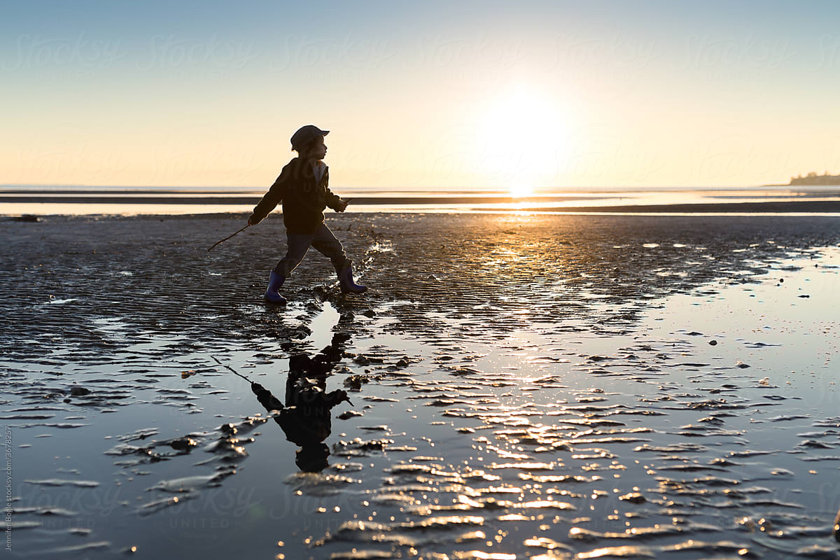 Boy walks on rippling sand at sunset