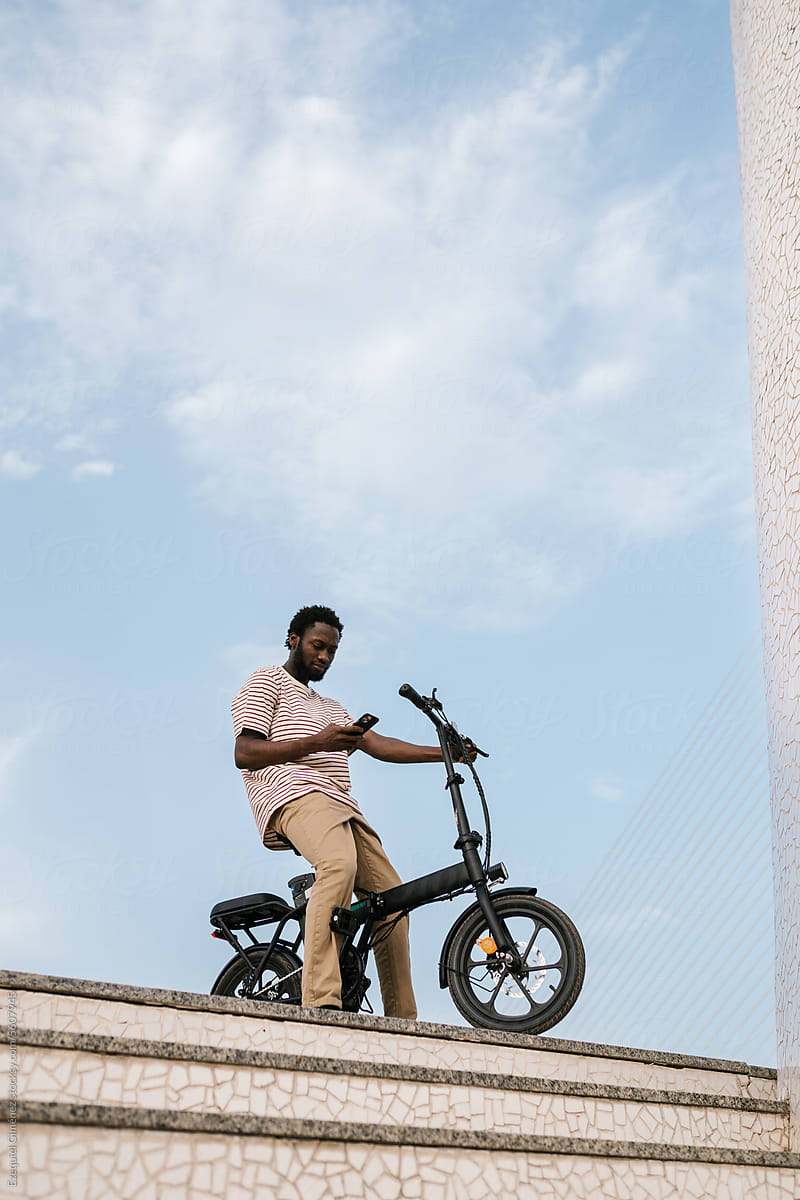 Black man using smartphone on e bicycle