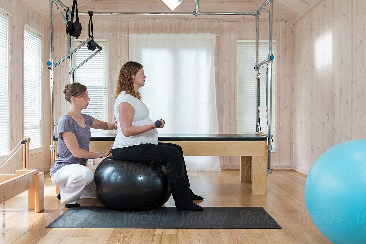 Pilates instructor guiding a pregnant woman through mental exercise whilst seated on a pilates ball