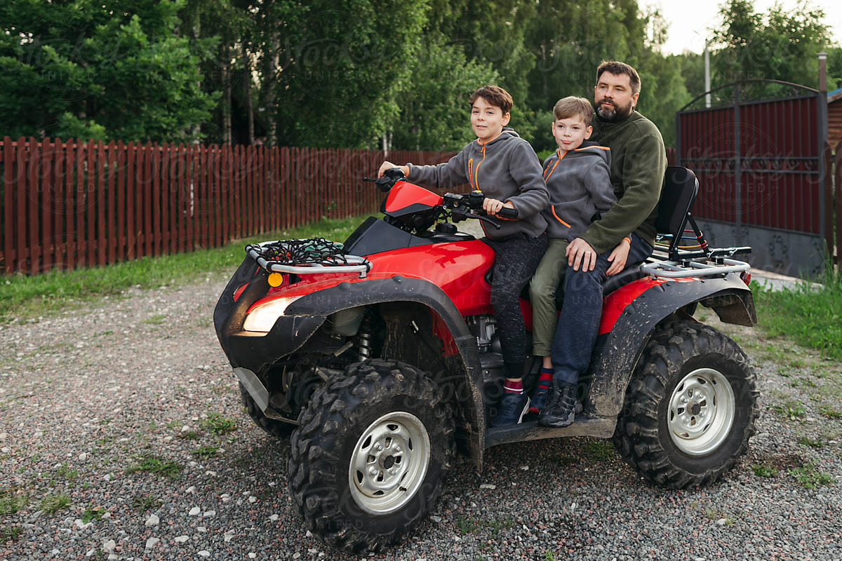 Little boys with dad on a quad bike in a rural area.