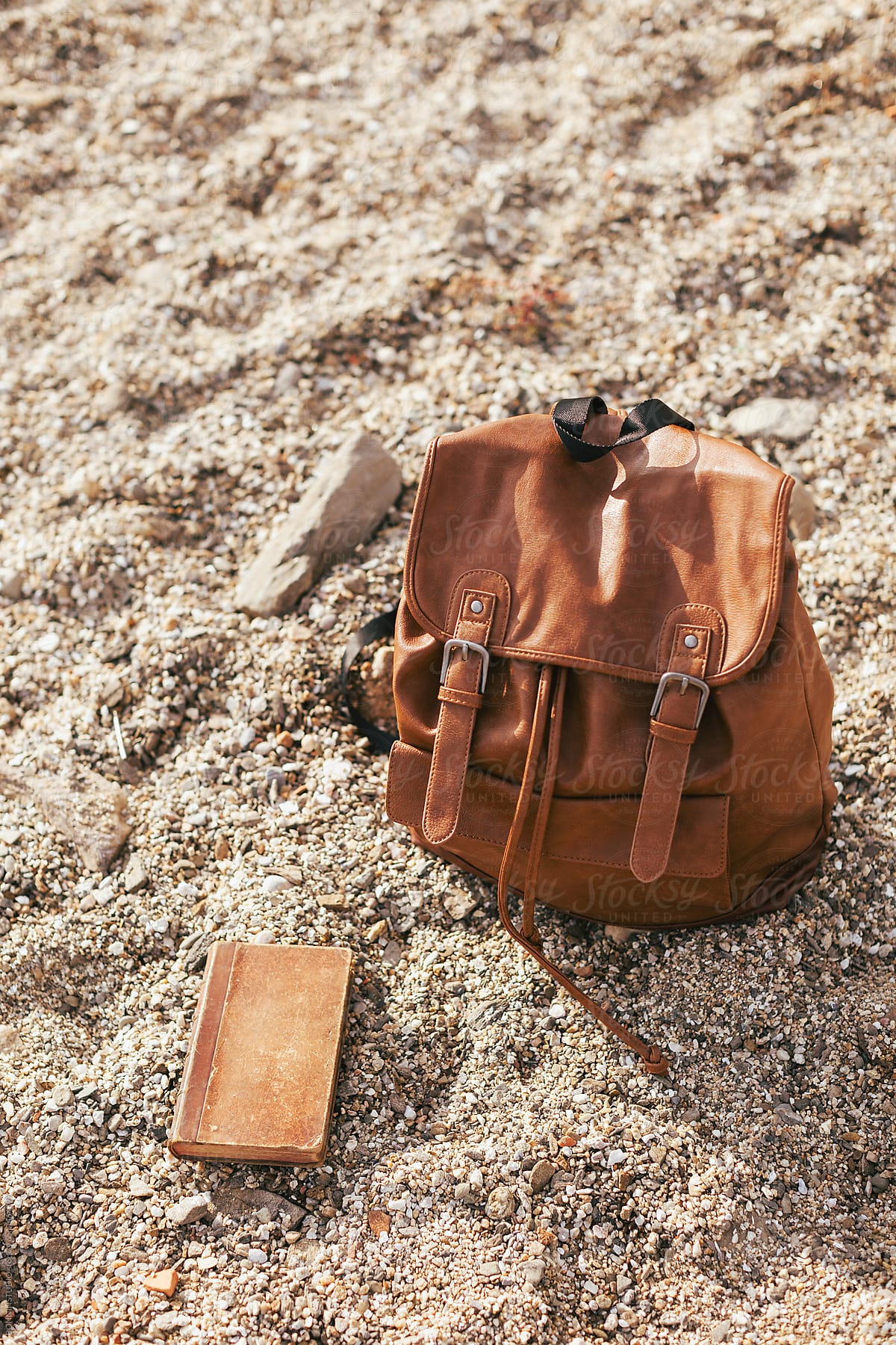 Leather backpack and old book in the sand of the beach.