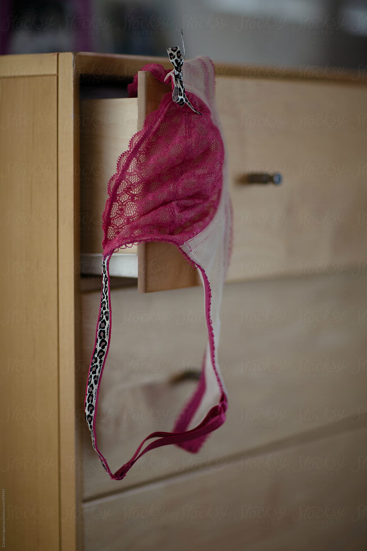 Pink lace bra hanging out of the top drawer of the dresser