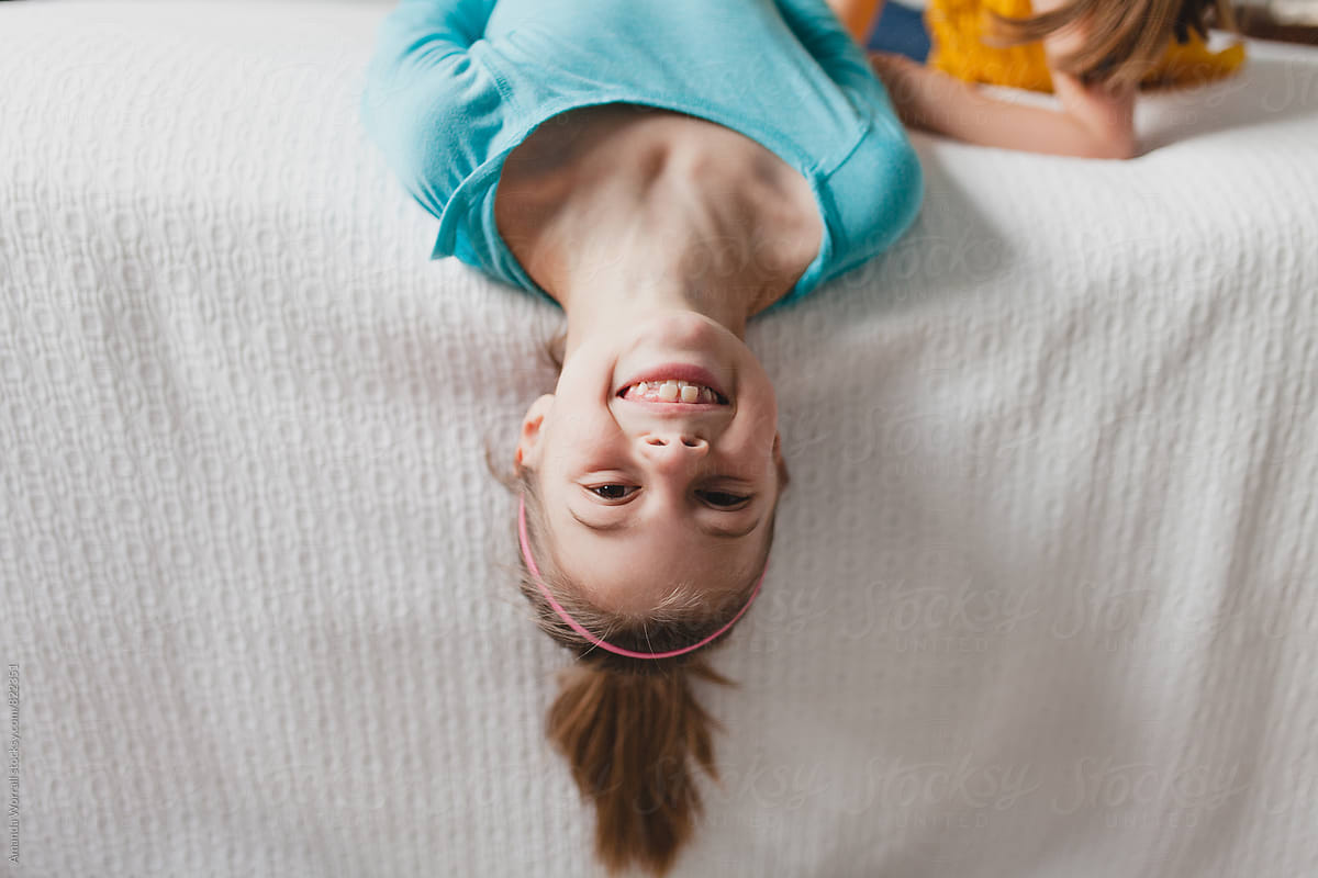 Happy, smiling girl flipped upside down at the edge of bed