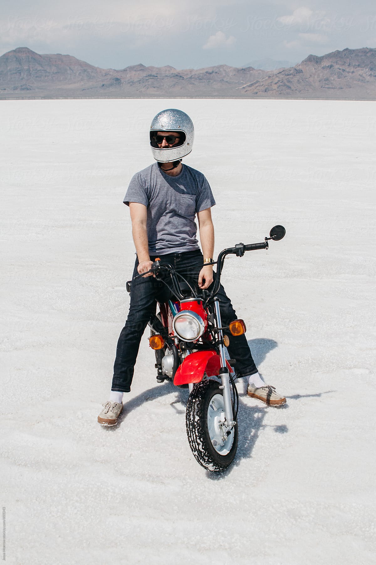 portrait of young male riding motorcycle and wearing helmet in desert sand salt flats