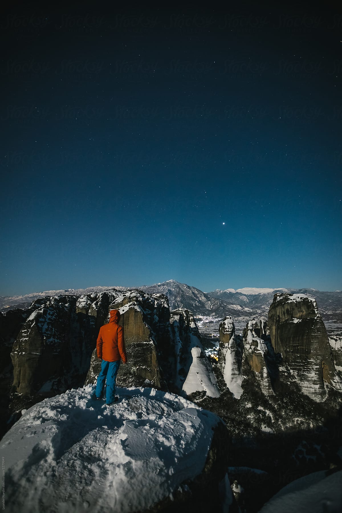 mountaineer standing on snowcovered rocks overlooking meteora at night