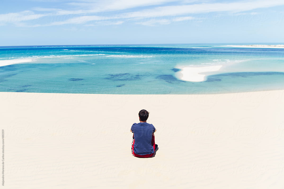 Young Man Sitting Down On The Sand Looking At The Ocean On An Exotic Tropical Beach With