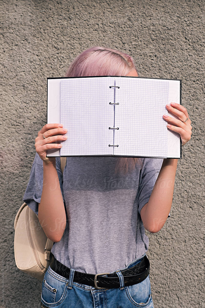 Girl with pink hair holding open notebook in front of face