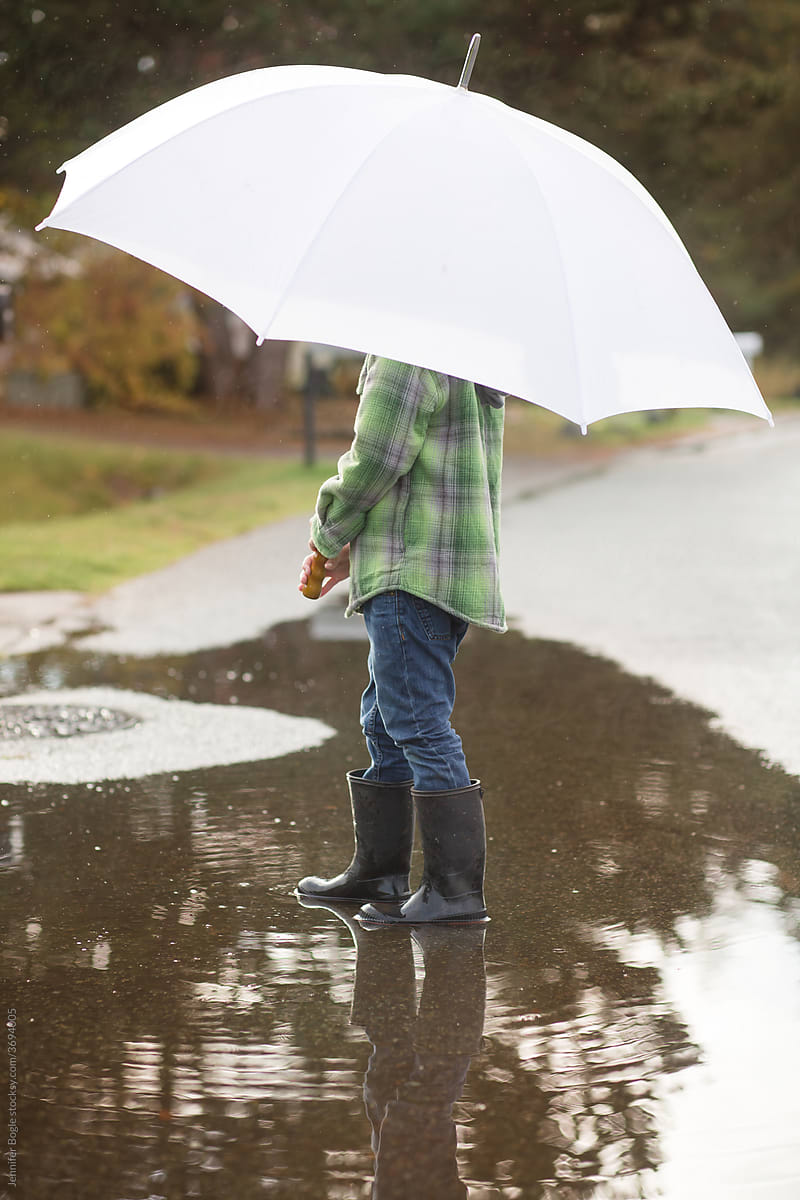 Boy with umbrella standing in puddle