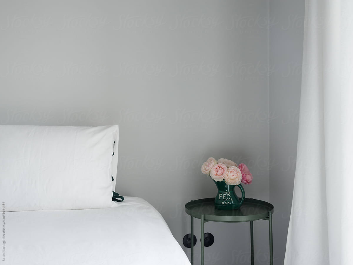 Minimalist bedroom with bed and bedside table with flowers next to a window