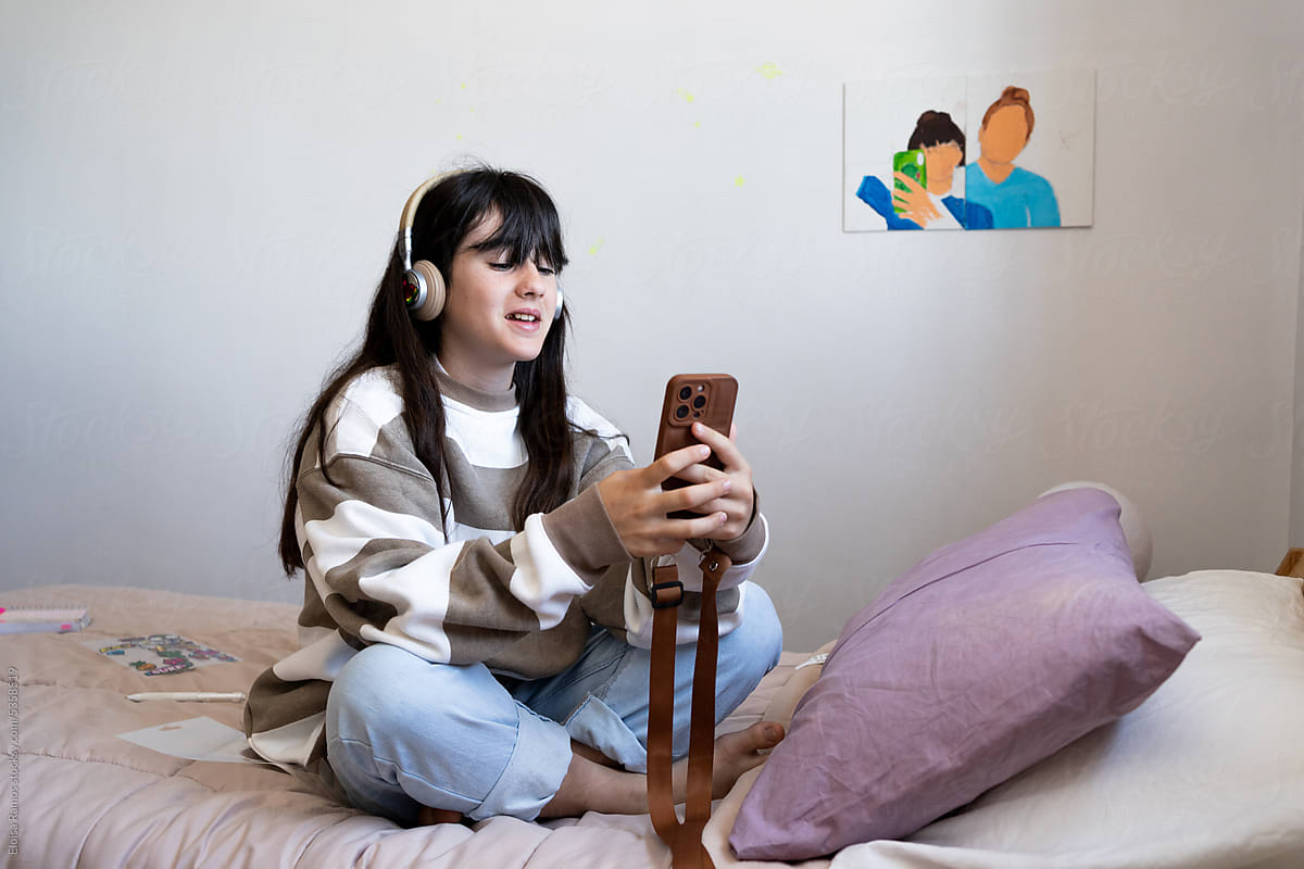 Teen Girl Chilling With Smartphone and headphones On Bed
