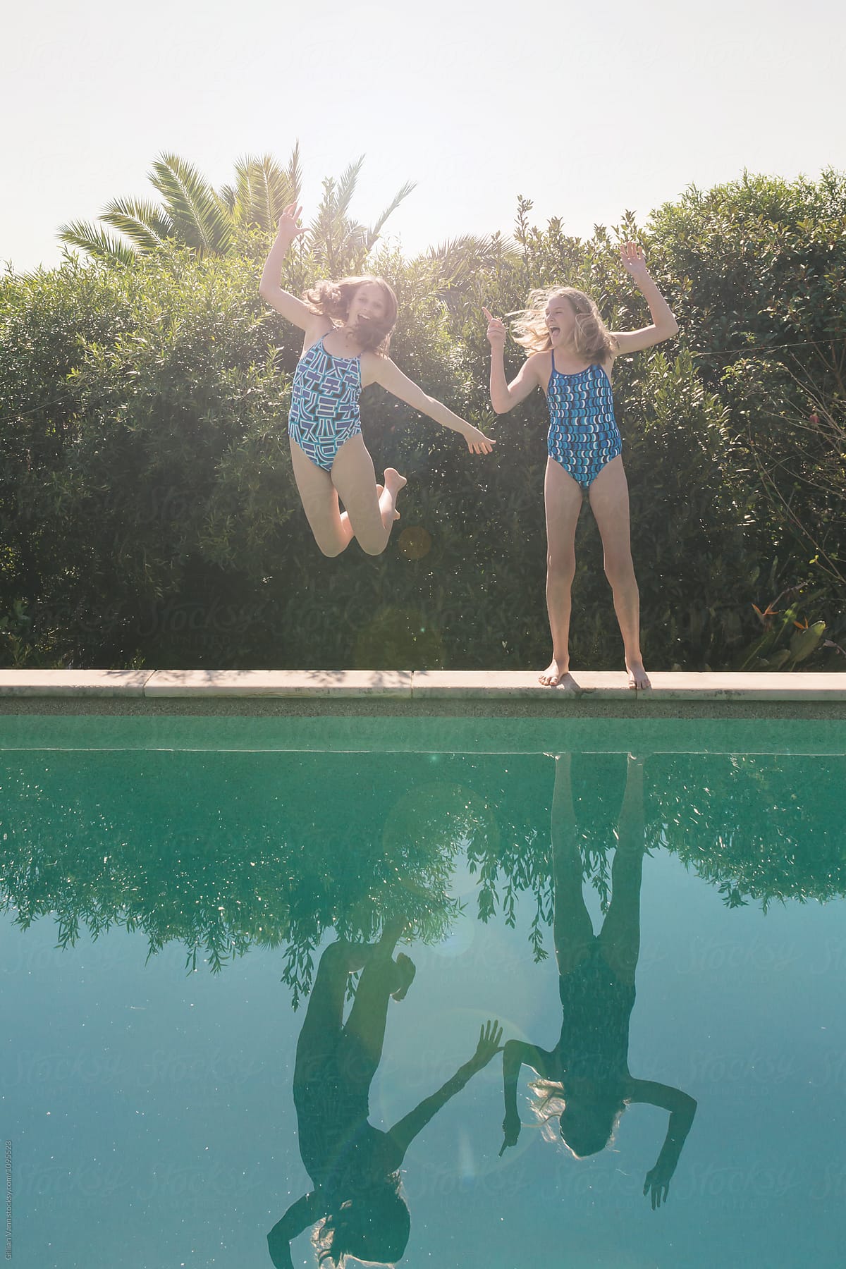 Teenage Girl Jumping Into A Swimming Pool With Her Sister Looking On