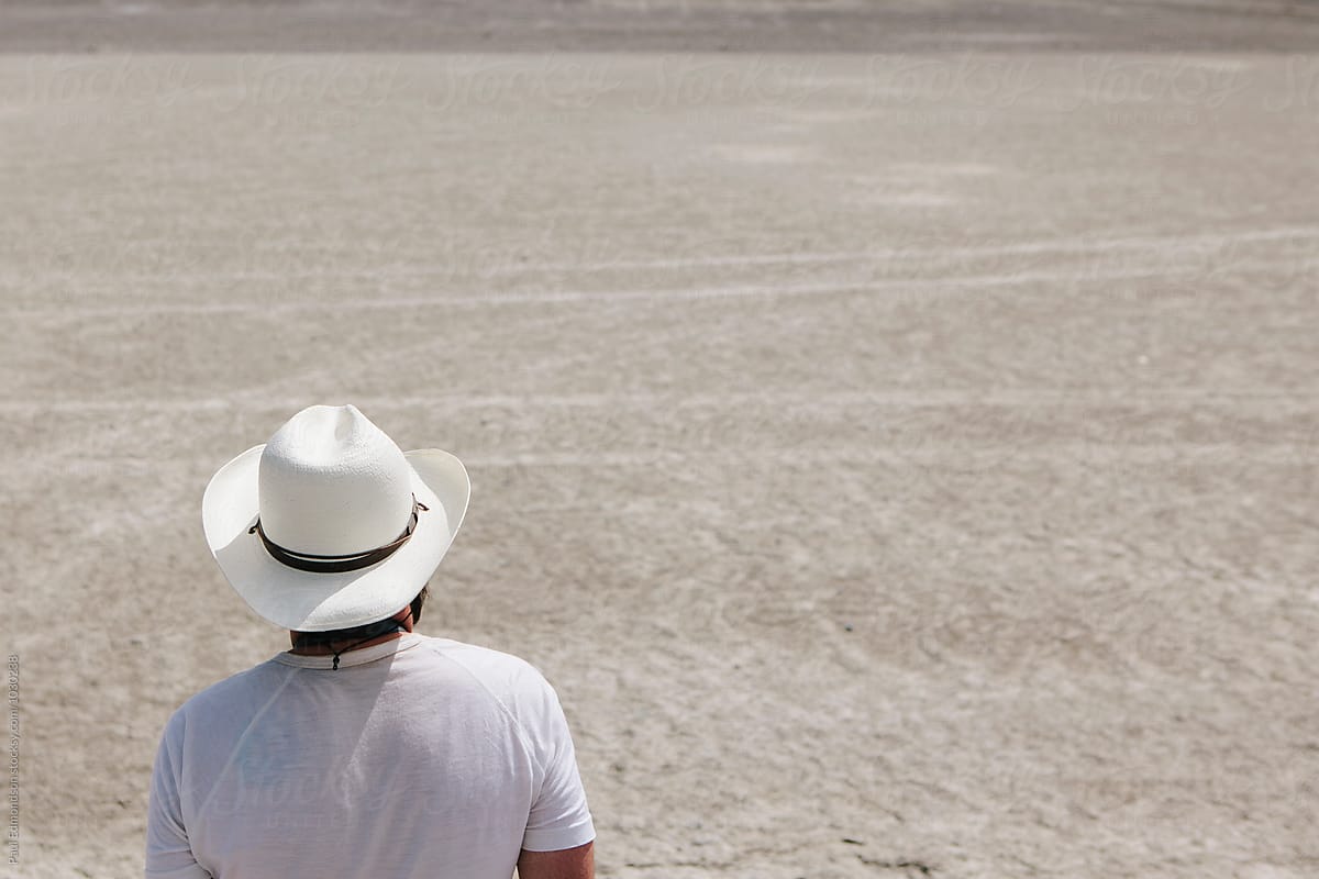 Backside view of man wearing white cowboy hat in desert