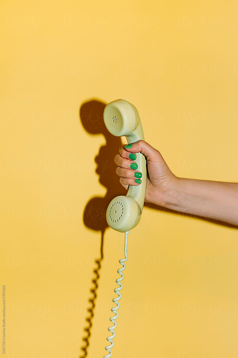 Hand holding a telephone in yellow background.