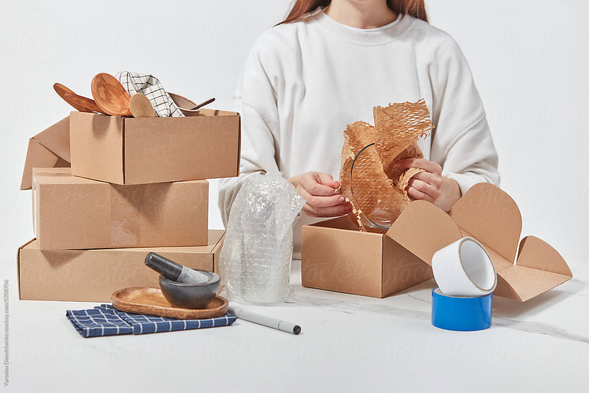 Unrecognizable girl putting dishware in cardboard packages.