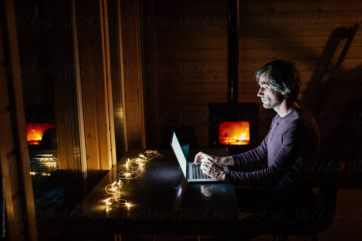 Writer working on laptop at night near fireplace