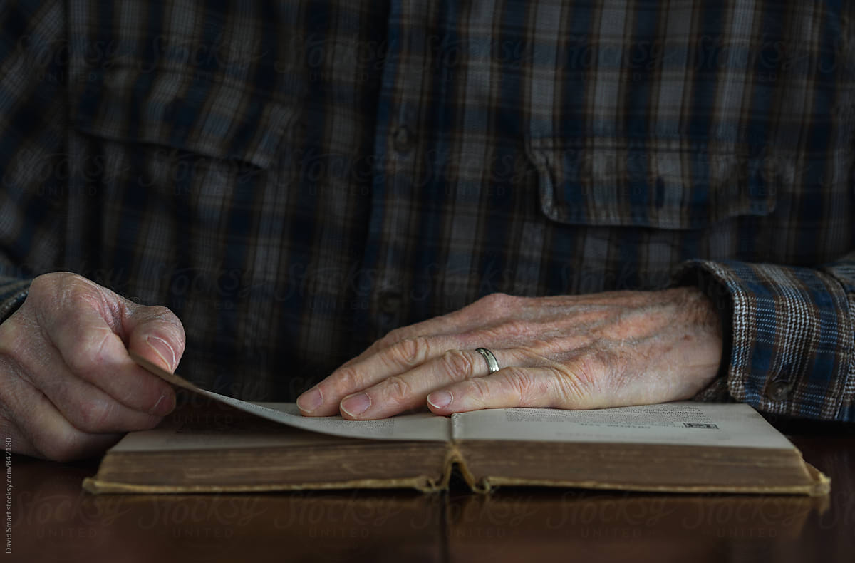Close-up, senior man\'s hands on pages of an old book.