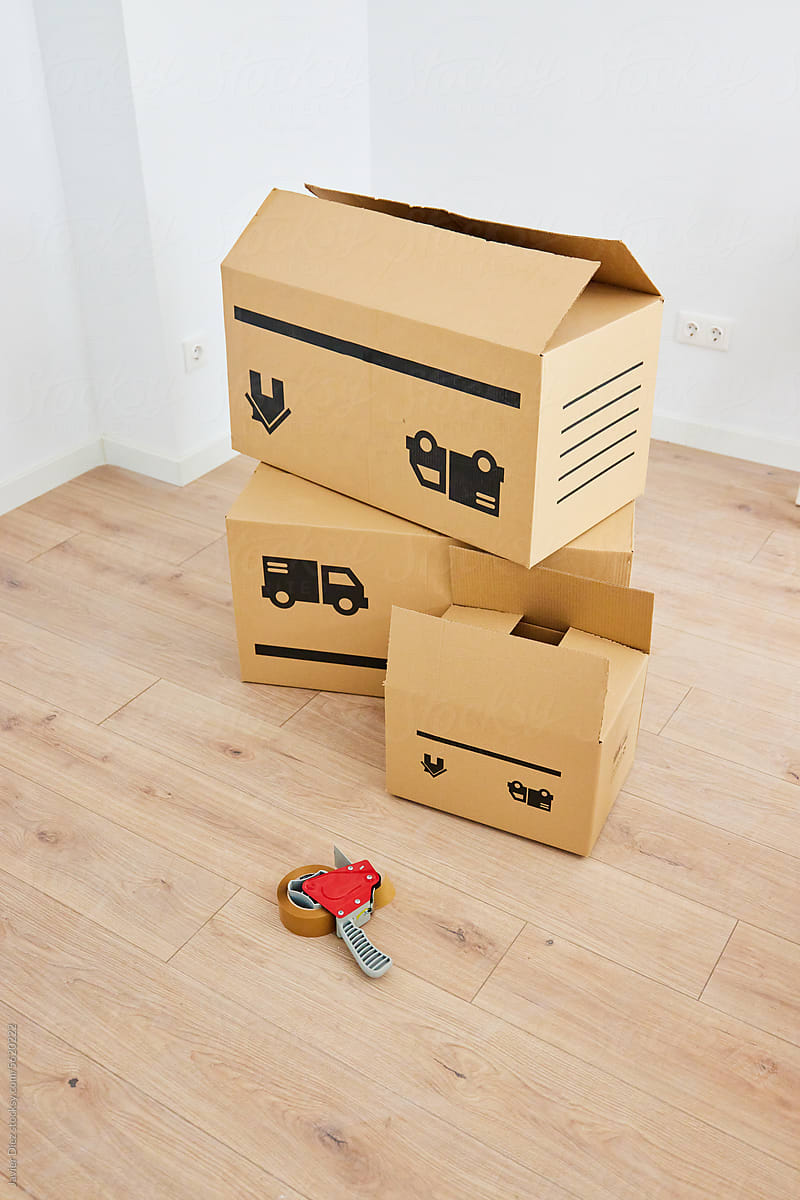 Carton boxes with cello tape and cutter in empty room