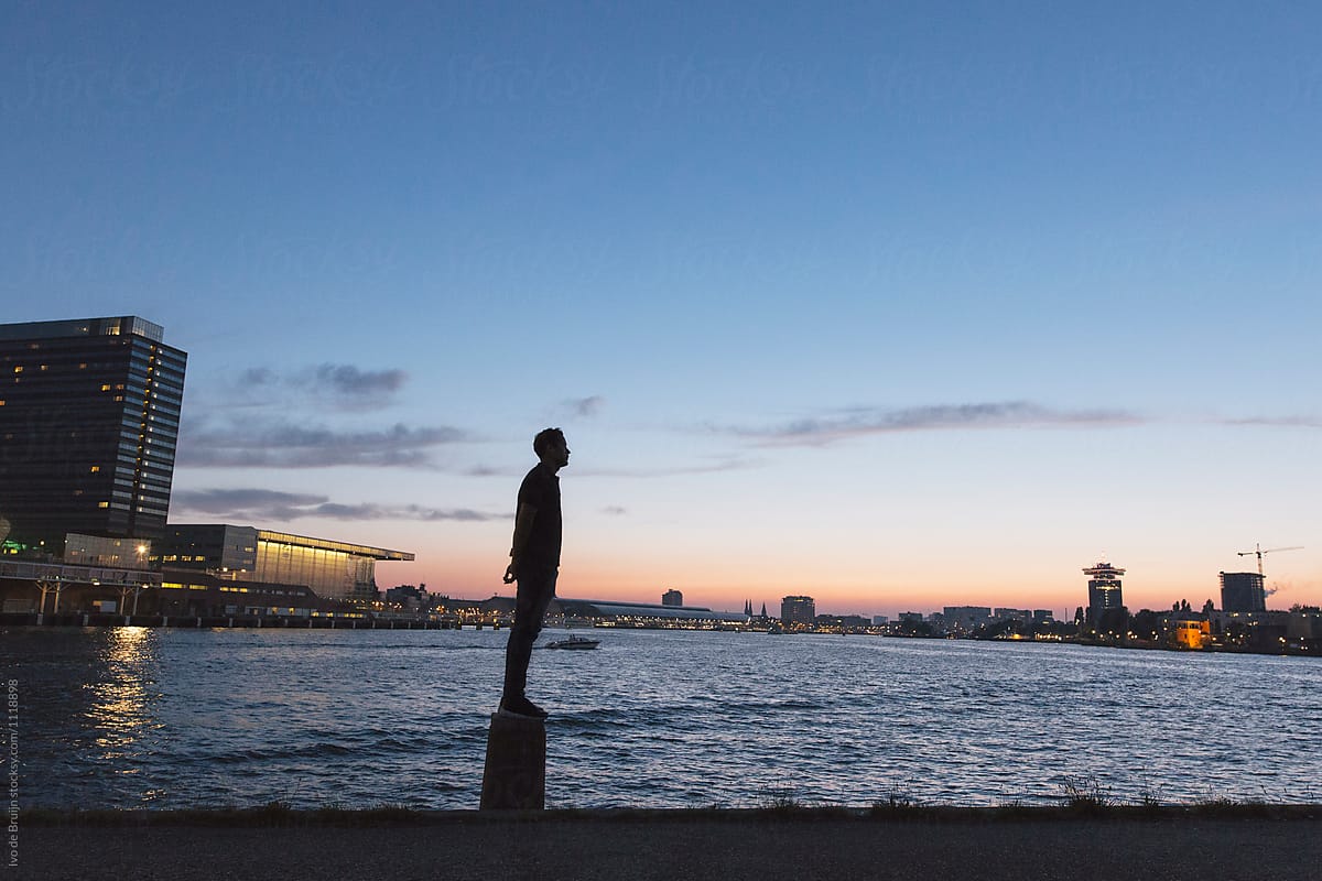 Man standing at the waterfront during dusk or sunset.