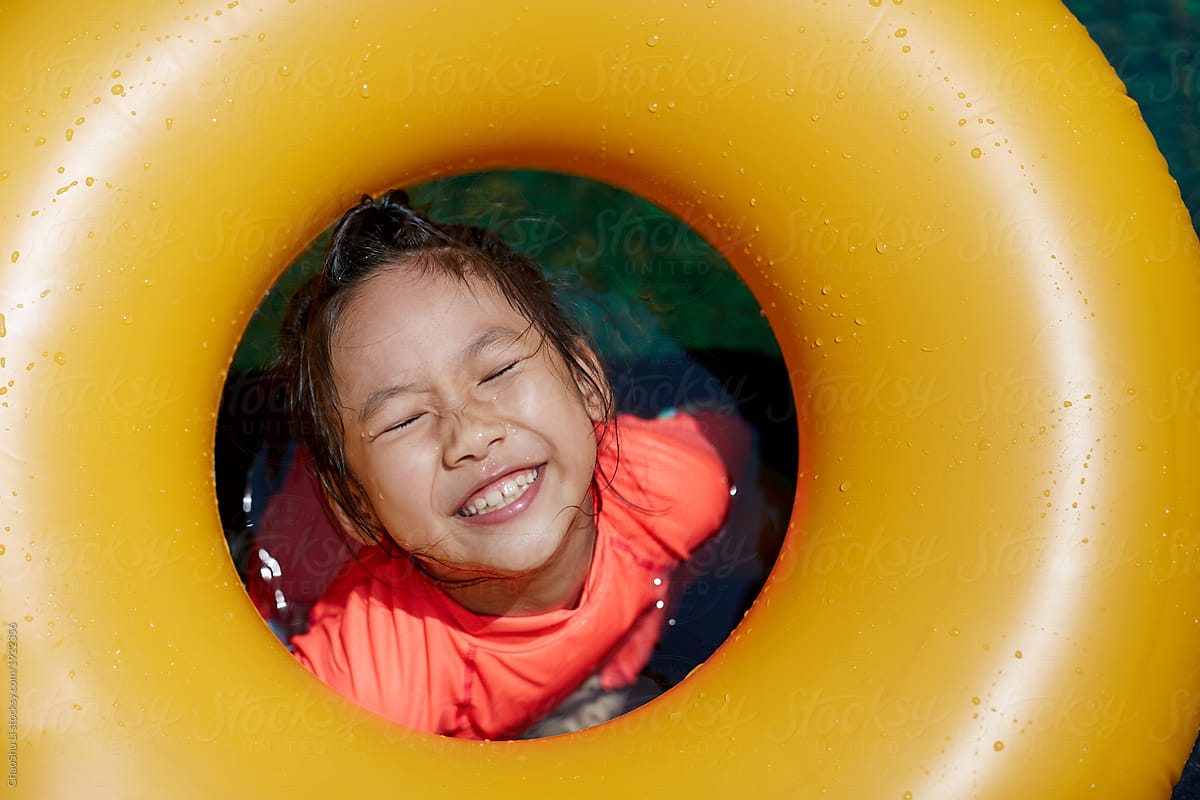 Cute Asian little girl swimming in outdoor infinity pool and holding colored life buoy.closeup