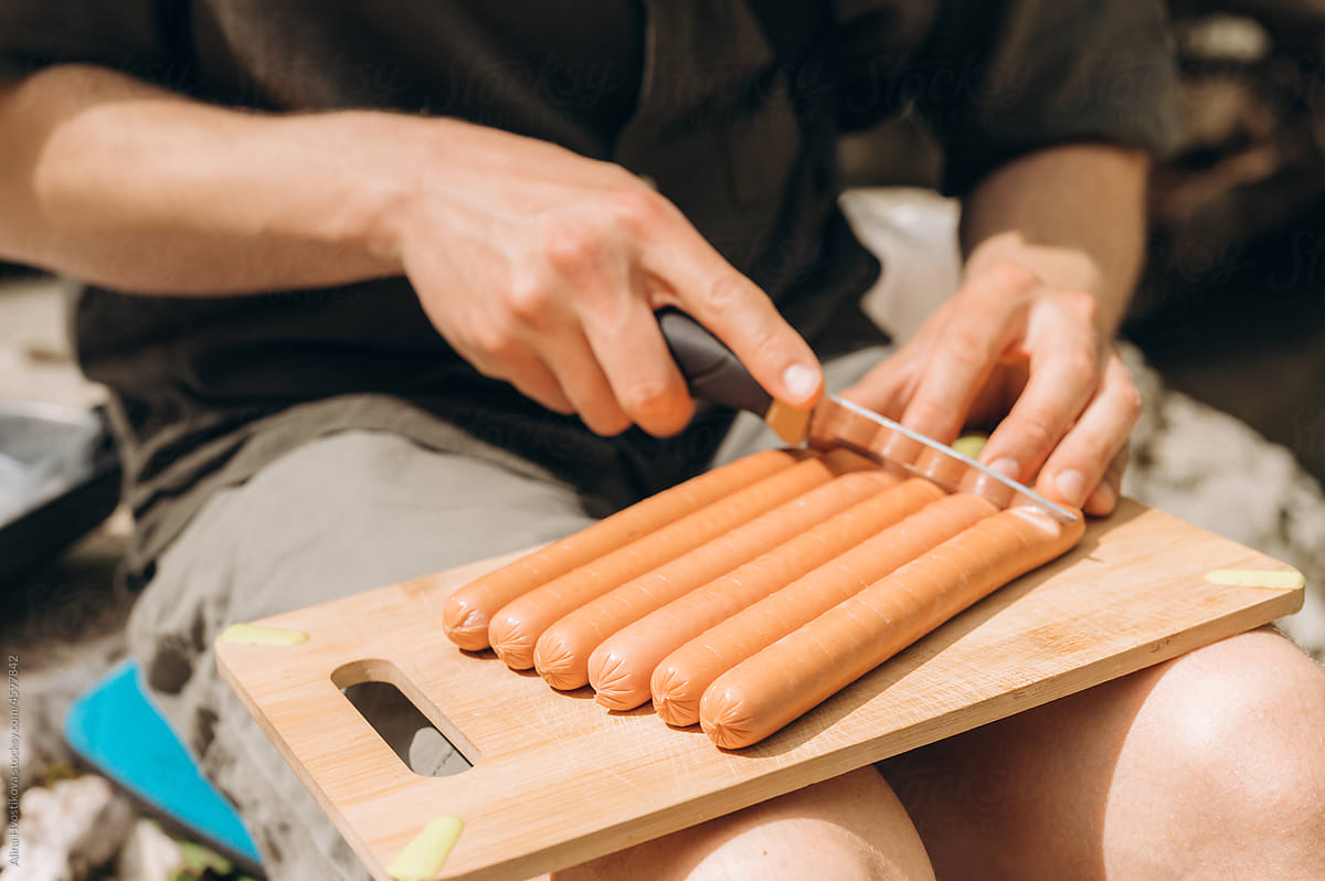 Crop traveler cutting sausages during picnic