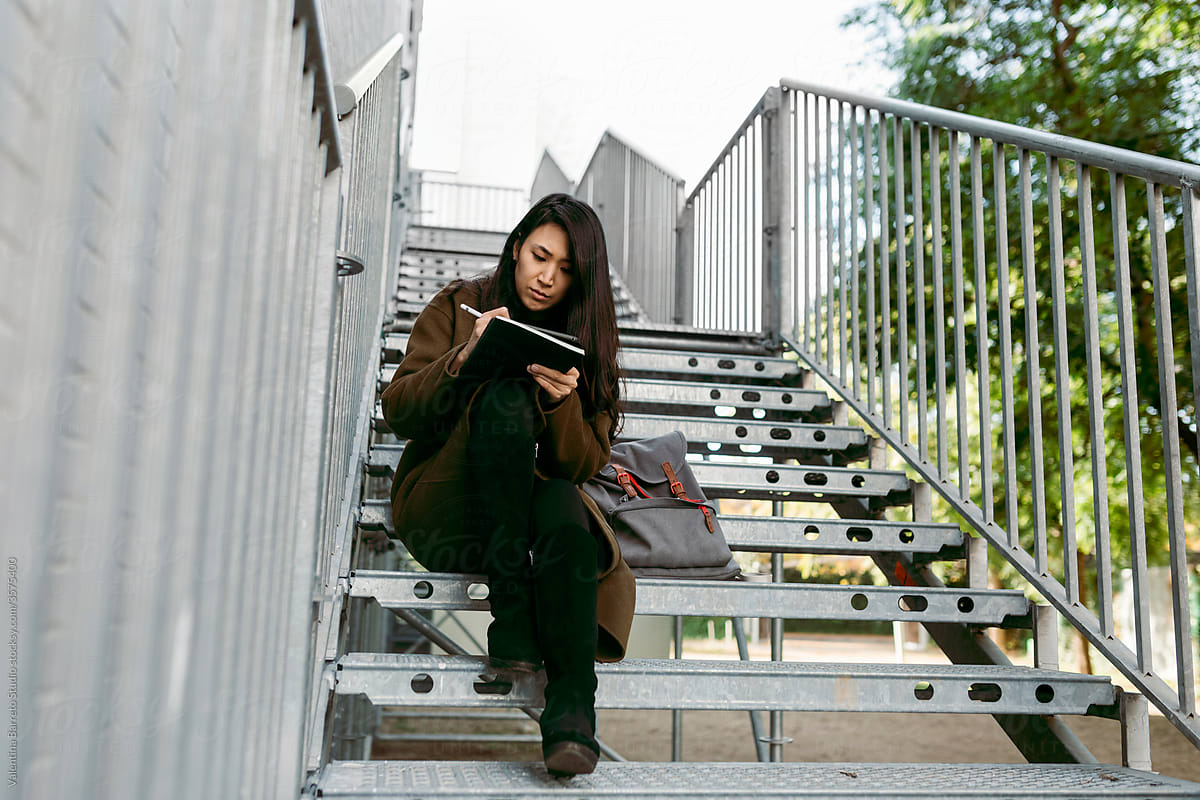 middle age woman drawing digital device sitting on building staircase