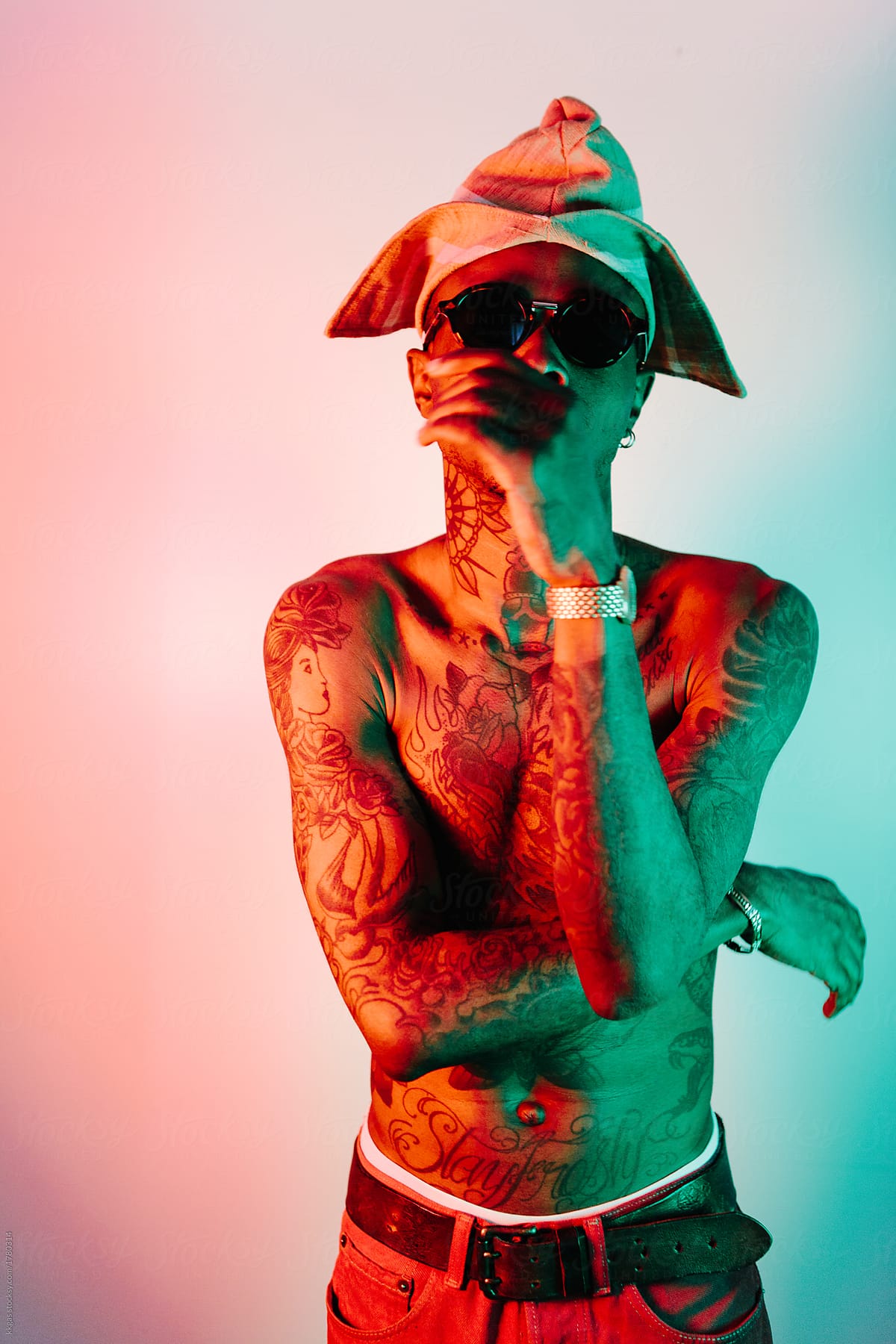Bare chested heavily tattooed man wearing a Yoruba hat with orange and green lighting
